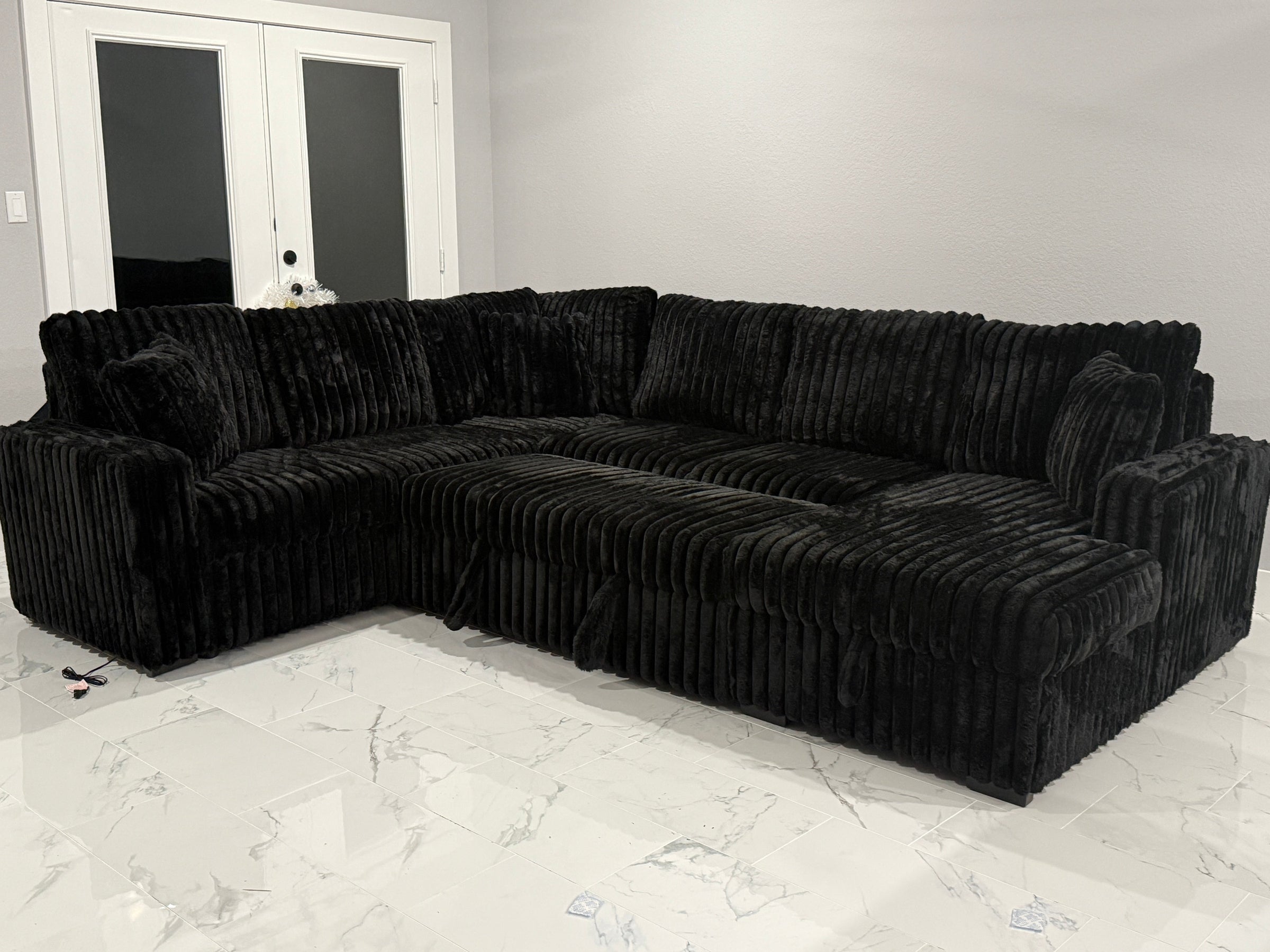 Black sectional sofa in a room with white walls and a marble floor.