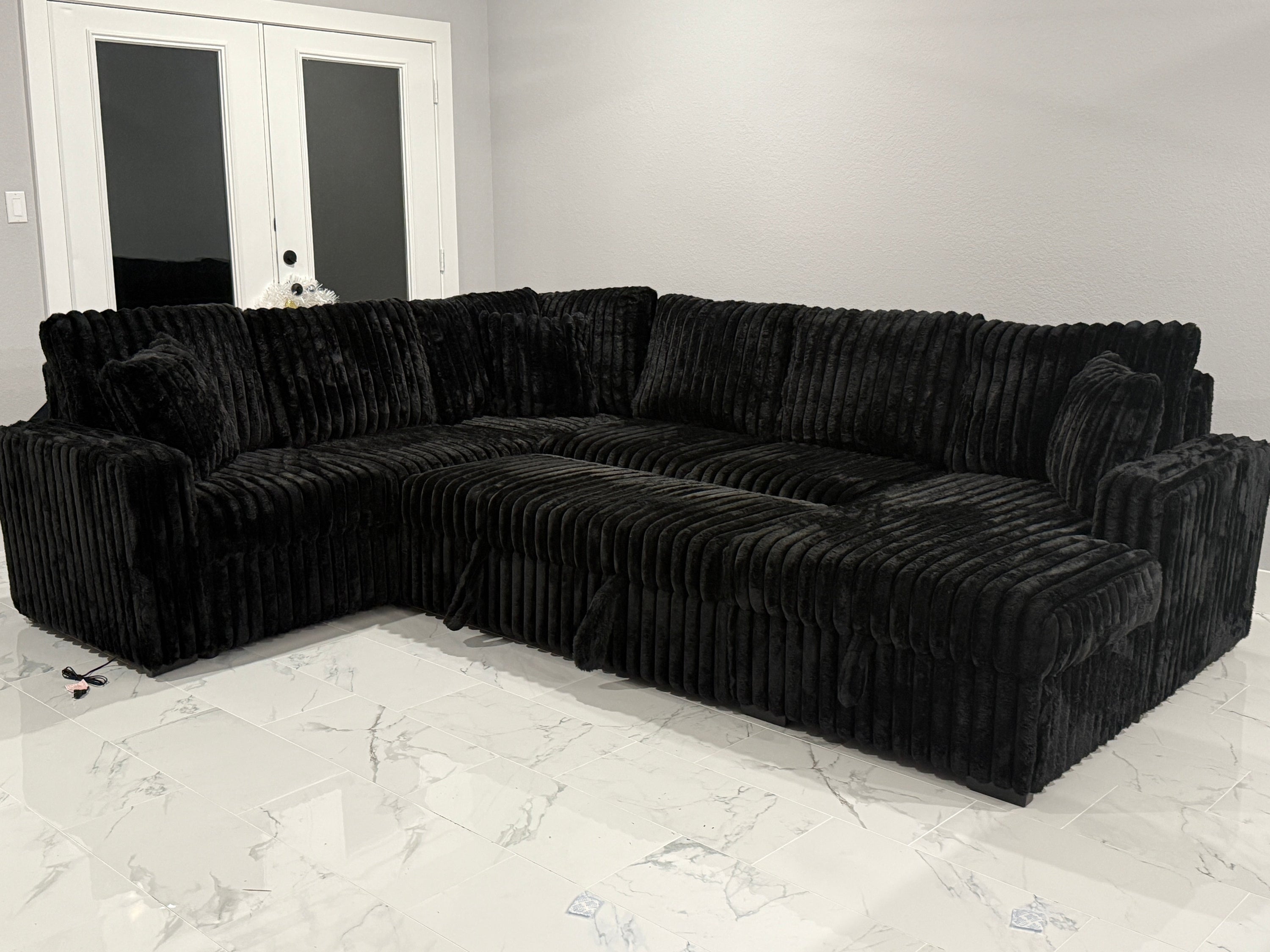 Black sectional sofa in a room with white walls and a marble floor.